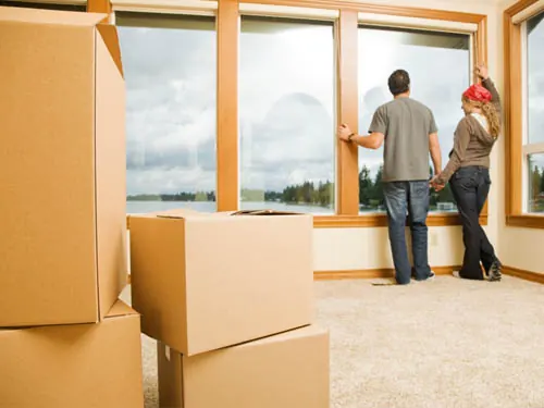 Casal observando a janela de um apartamento com caixas de mudança